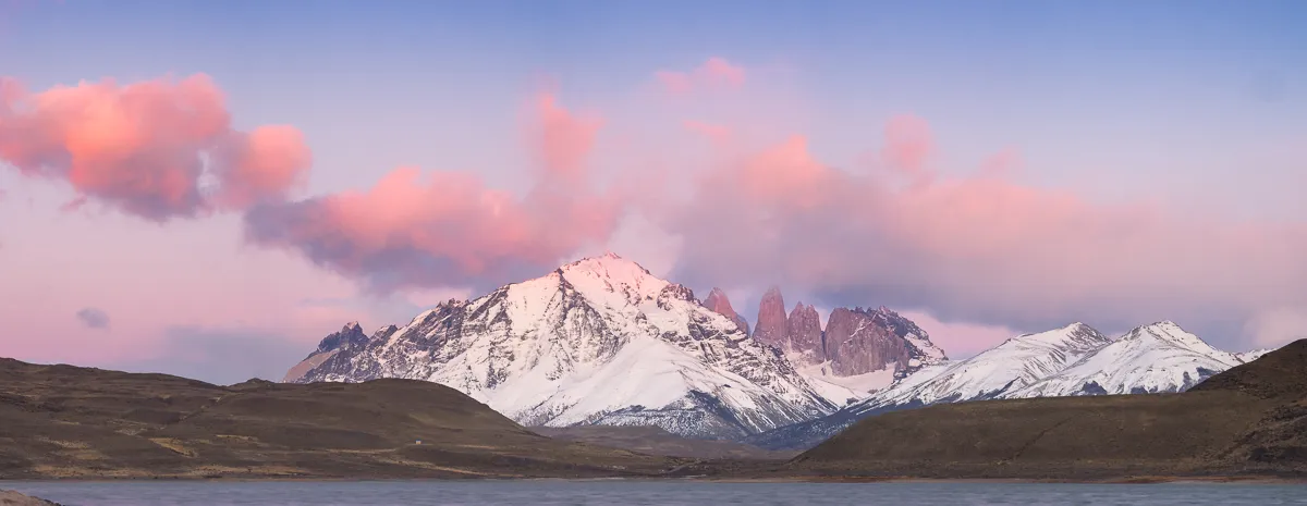 El Macizo del Paine y las Torres nevados bajo nubes rosadas, sobre un lago del Parque Nacional Torres del Paine